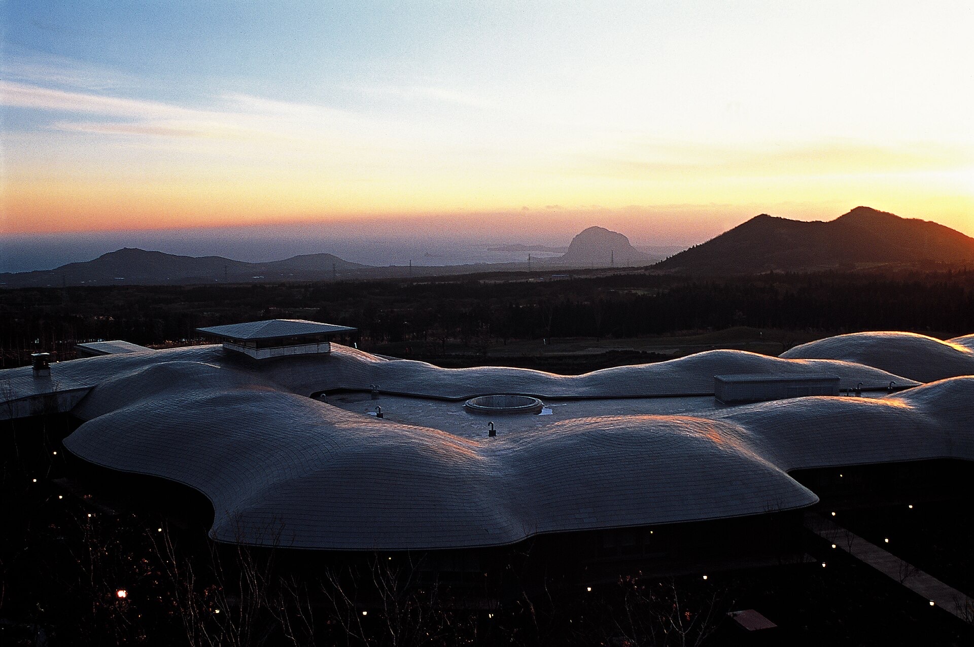 Podo Hotel's grape-cluster roofline against a dusk sky and Jeju's volcanic cones